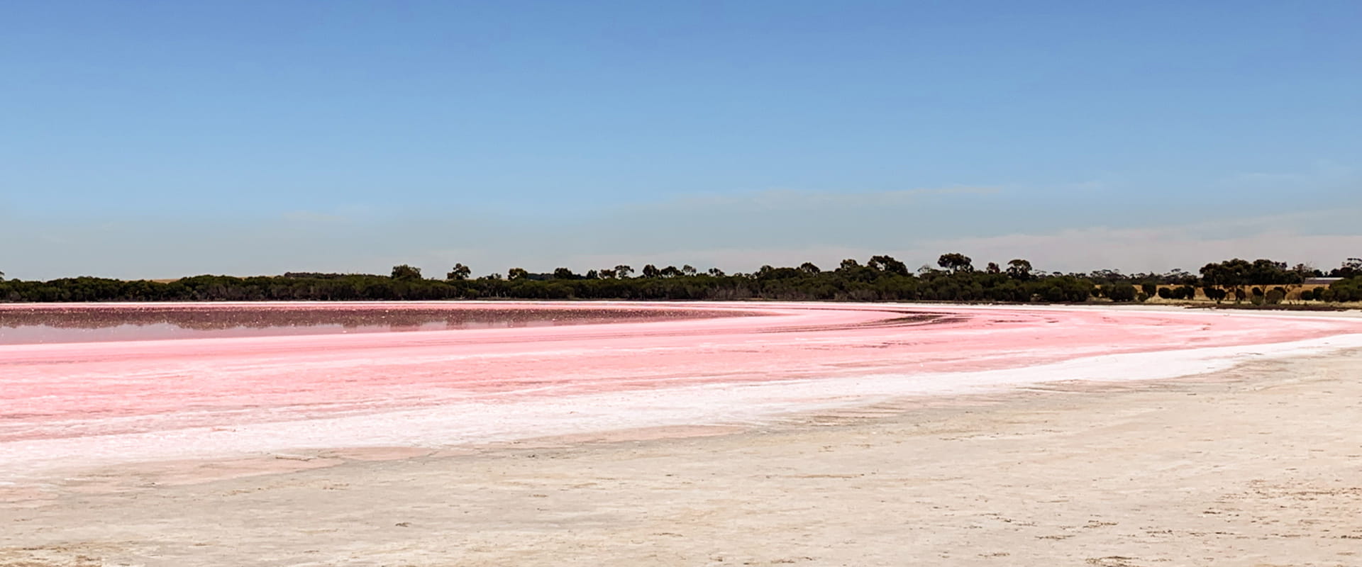A lake that is low in capacity, with the water's edge surrounded in pink salt.