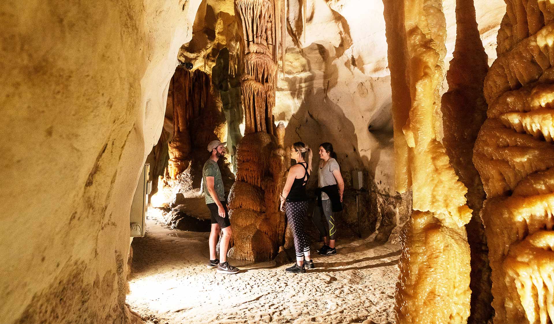 Three friends chat together around a rock formation in an underground cave in Lower Glenelg National Park.