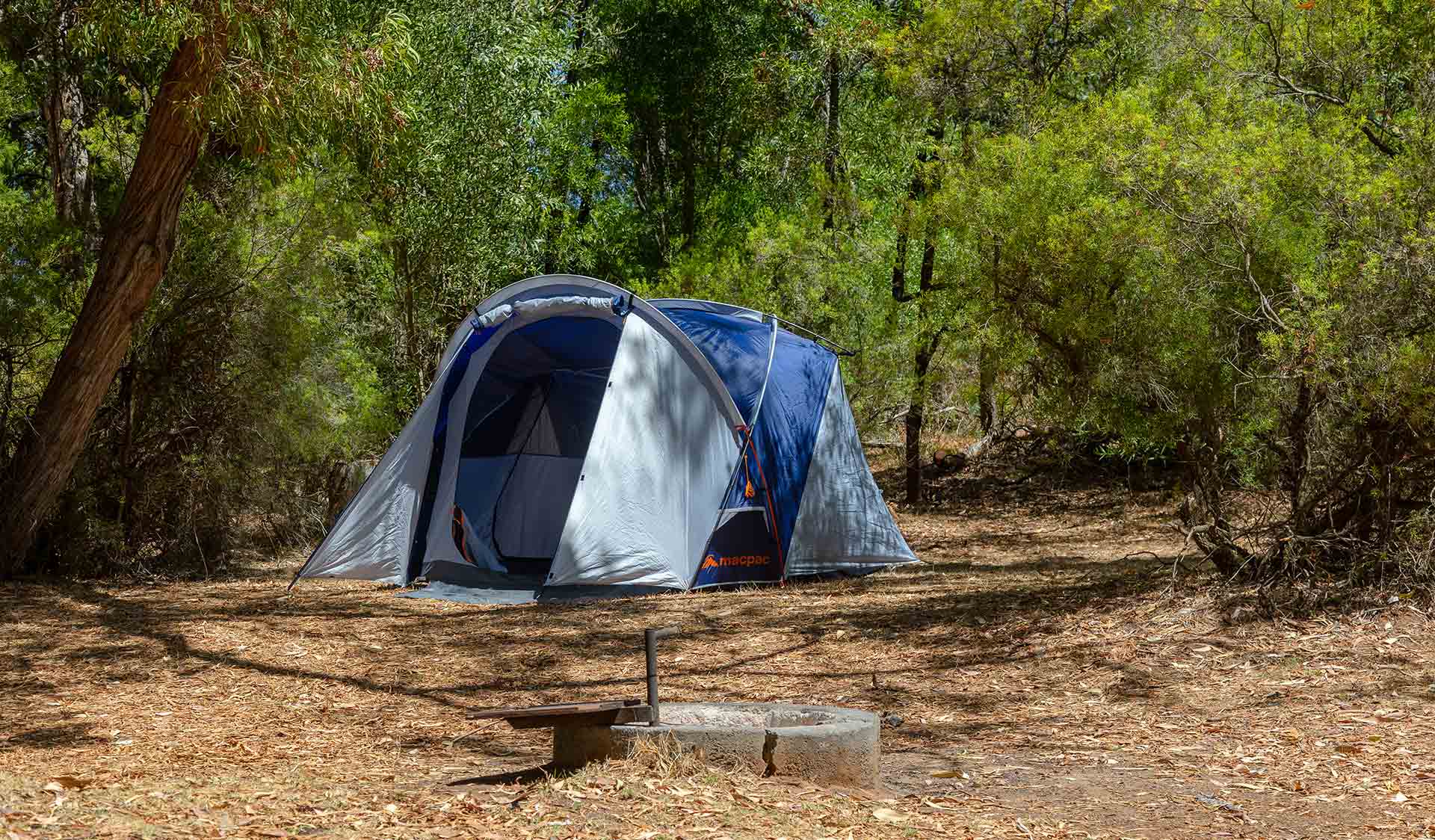 A tent and fireplace set among green trees at Princess Margaret Rose Caves Campground at Lower Glenelg National Park