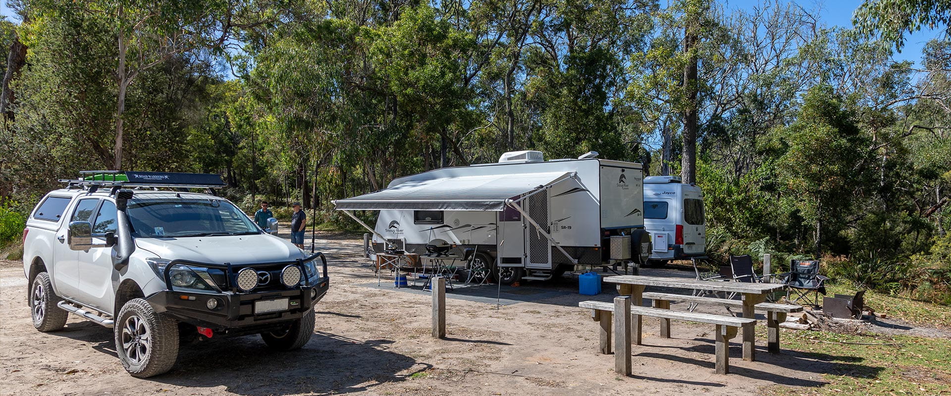 A white ute parked next to two white caravans.