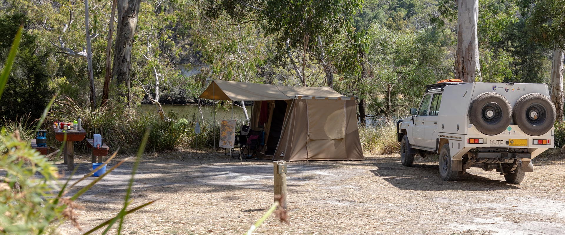 A white ute parked to the right of a canvas tent setup on the banks of the Glenelg River.