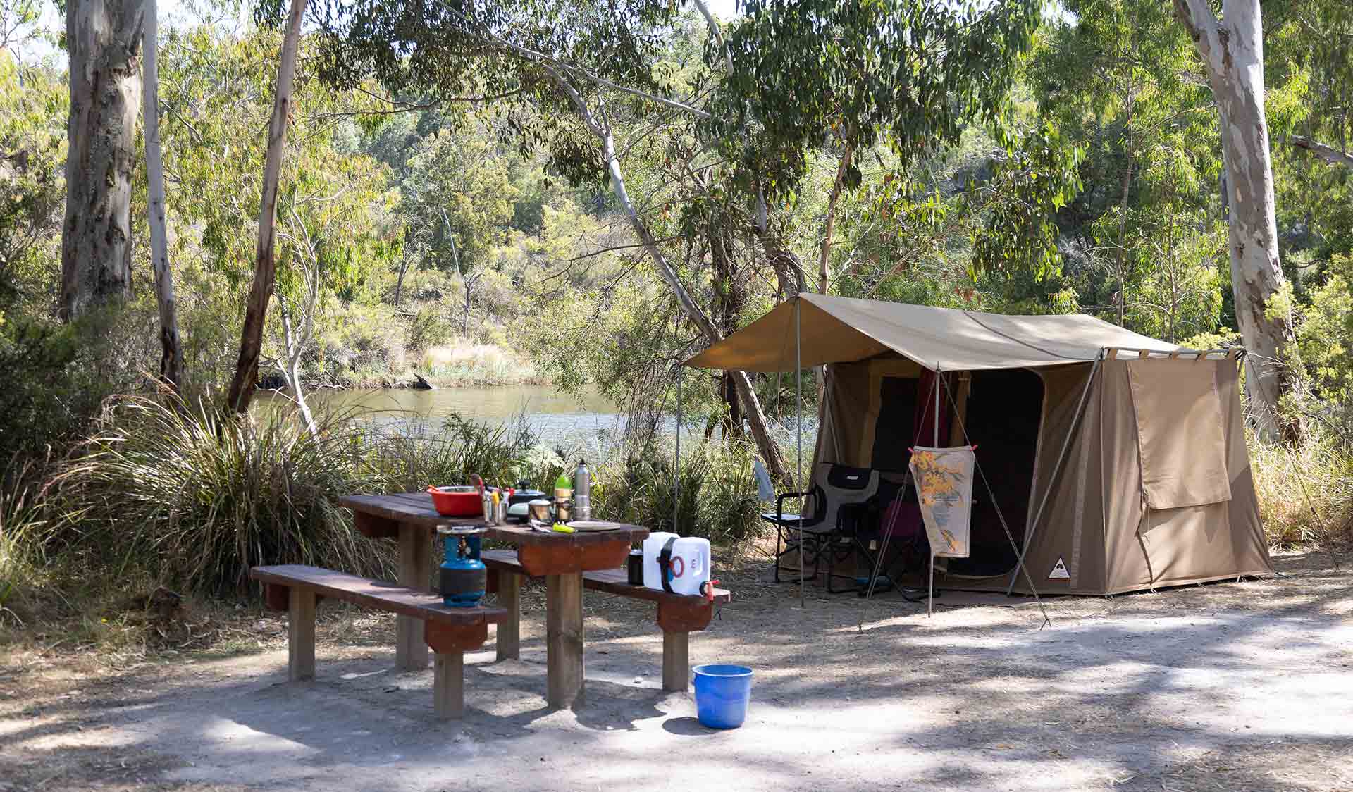 A canvas tent and picnic table in front of the river at Red Gum Landing campground at Lower Glenelg National Park