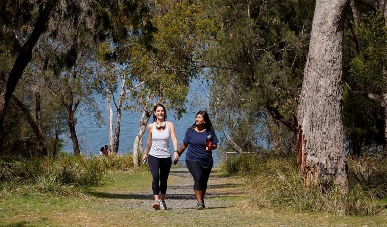 Two friends in activewear walk away from the lake.