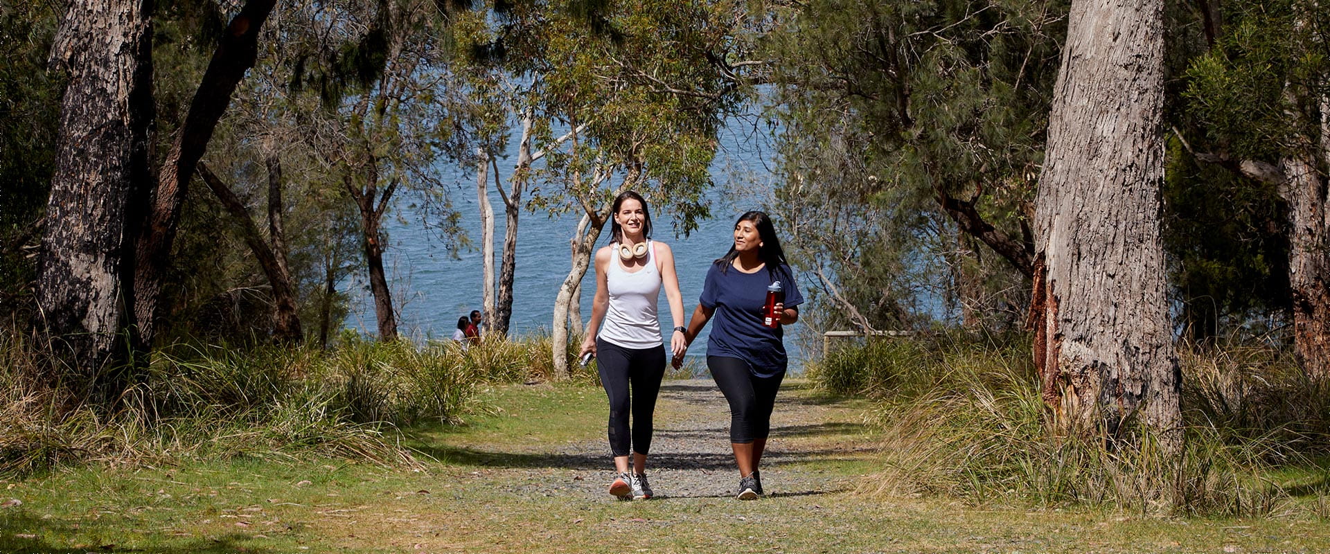 Two women in activewear walk along a path heading away from the lake.