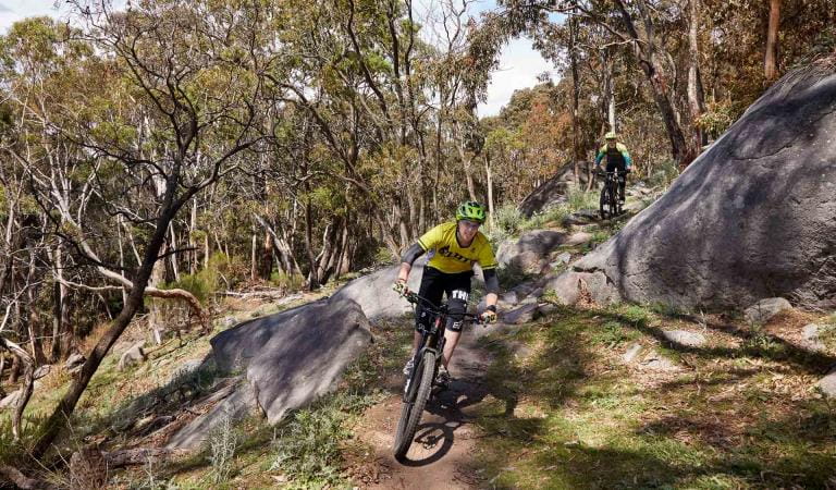 A mountain biker leading another down a rocky trail at Lysterfield Park