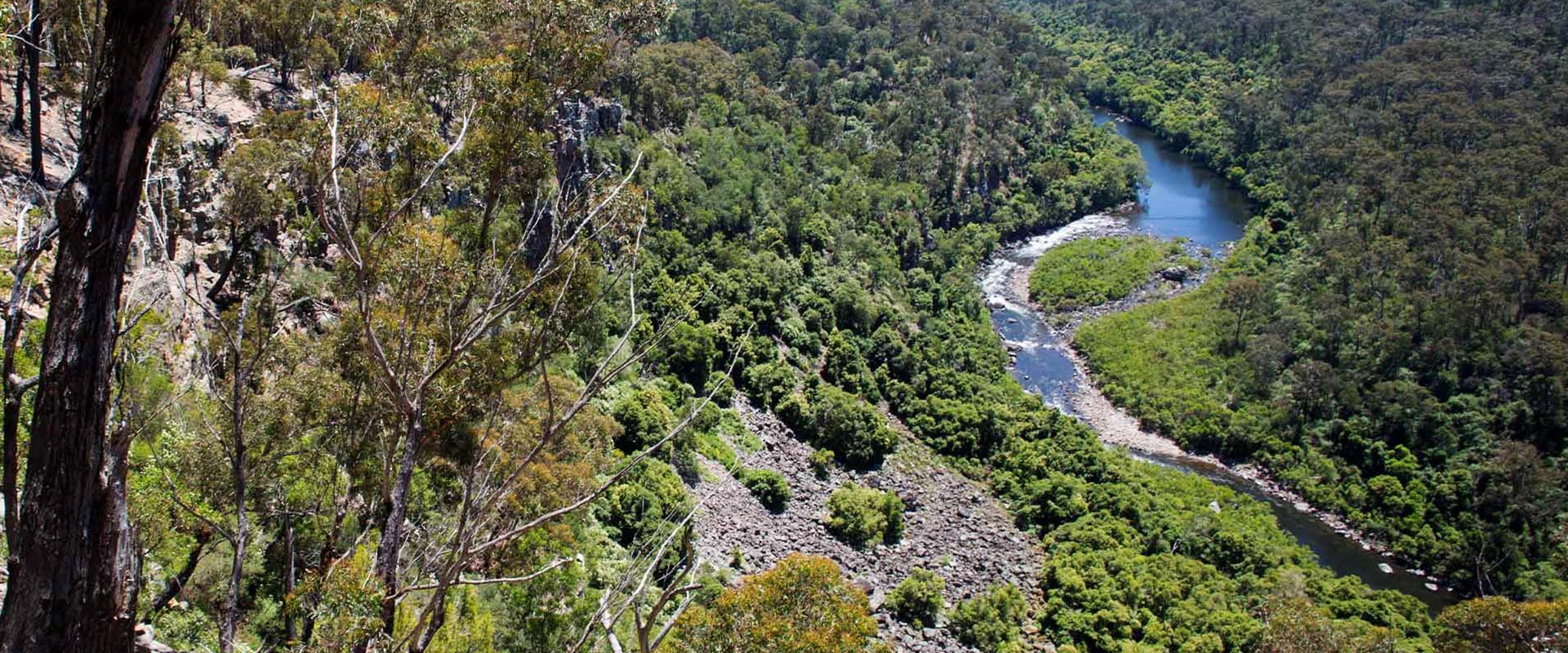 A spectacular view looking down over a long winding river surrounded by hills in dense rugged bushland