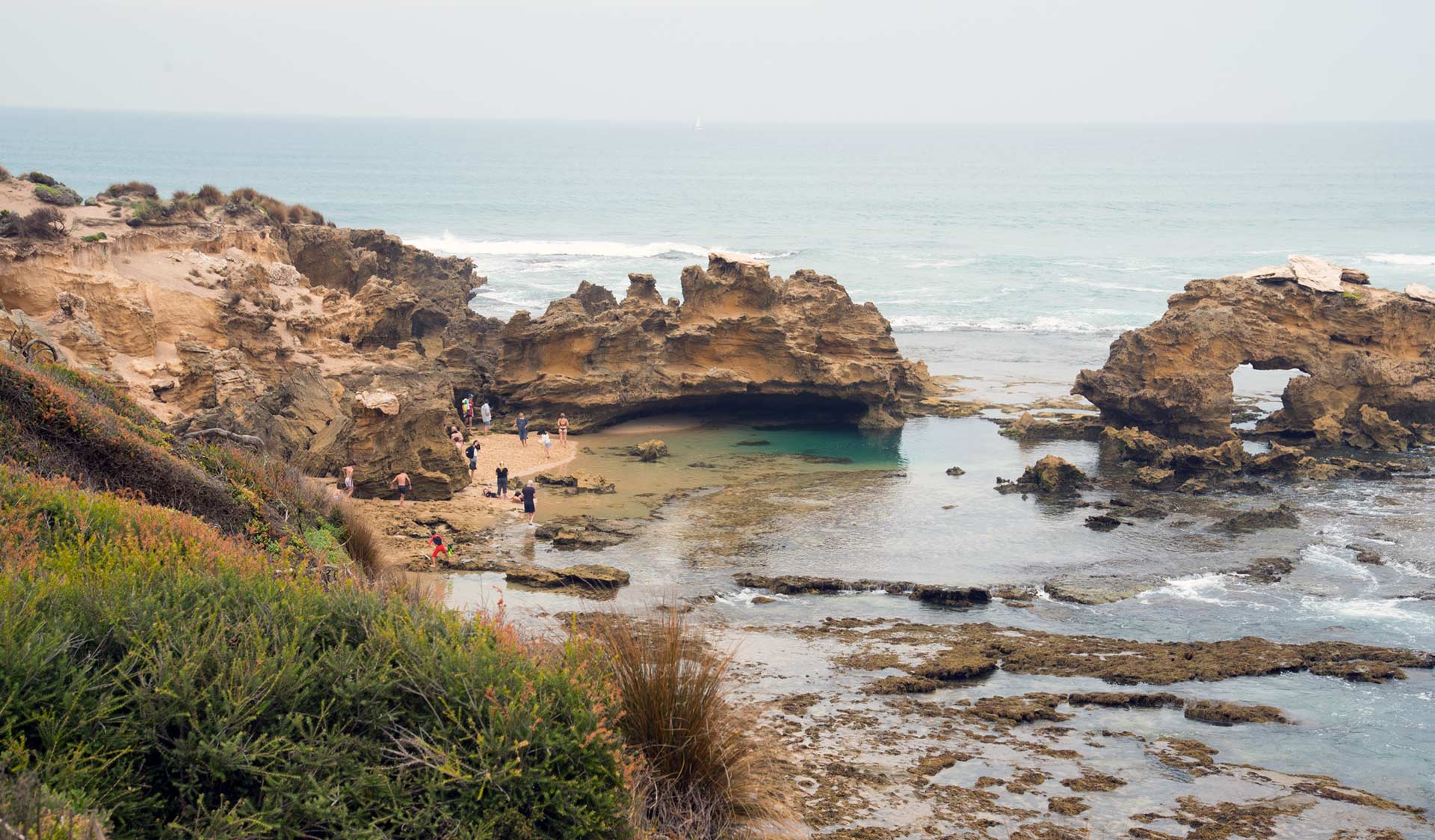 People play on the beach and explore the rock pools among the sandstone formations at Rye Back Ocean Beach.