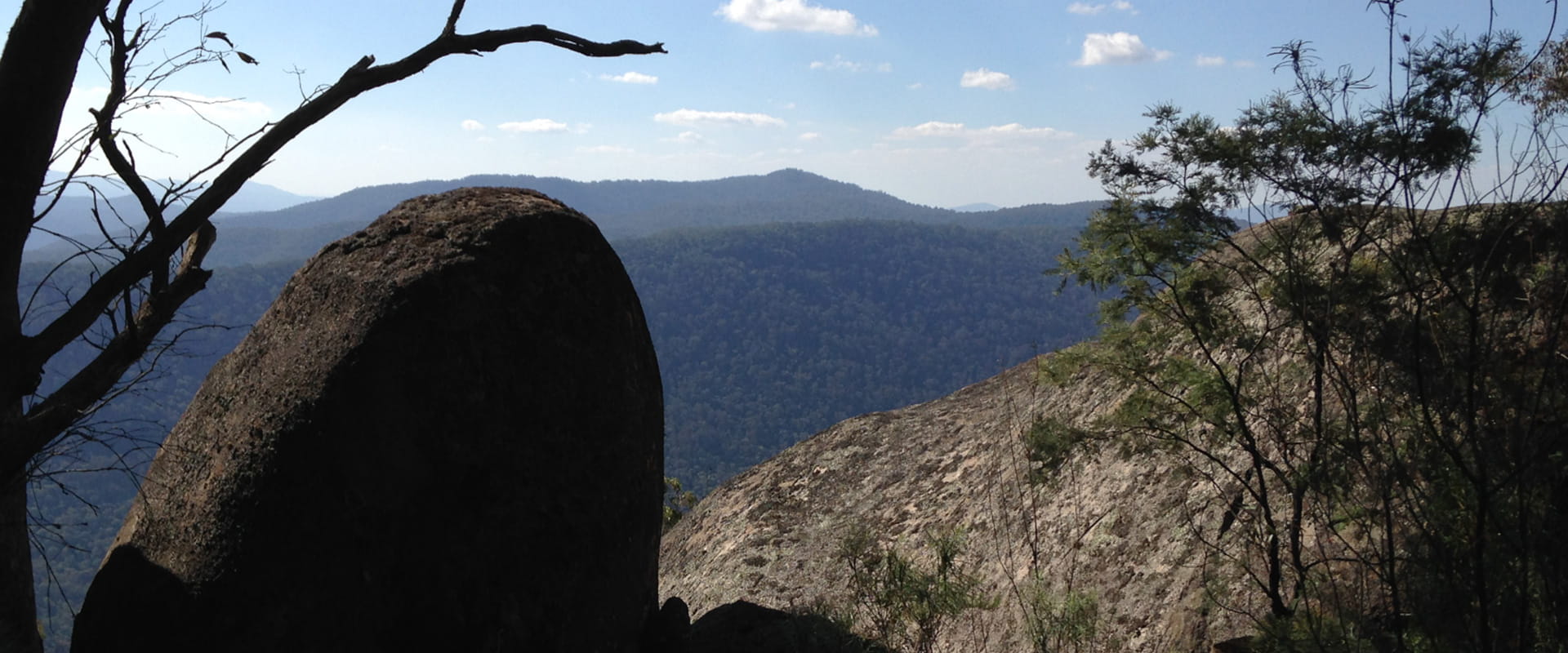 A view of a mountain range covered in dense trees from behind a large boulder