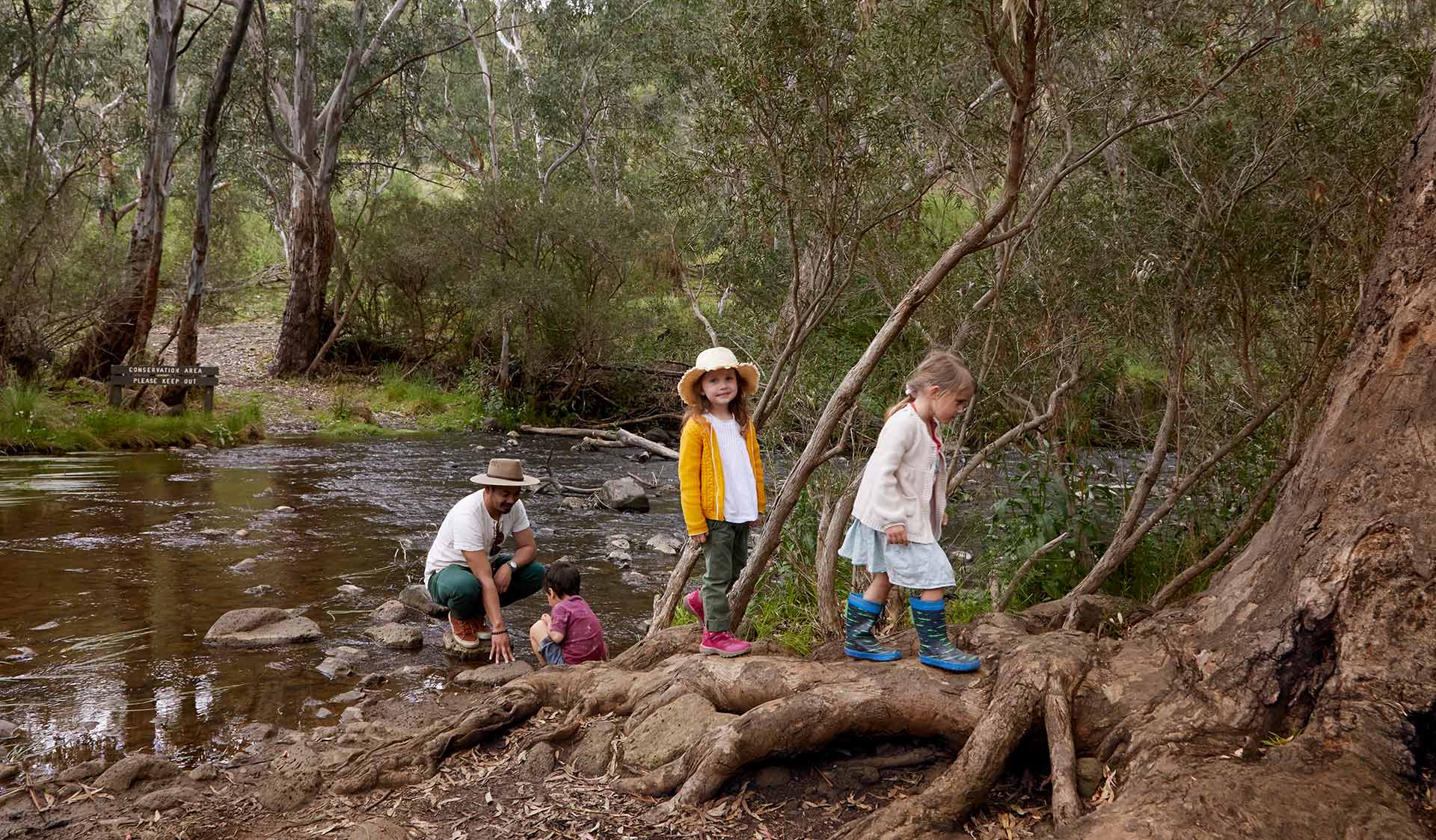 Three small children and a father cross a creek.