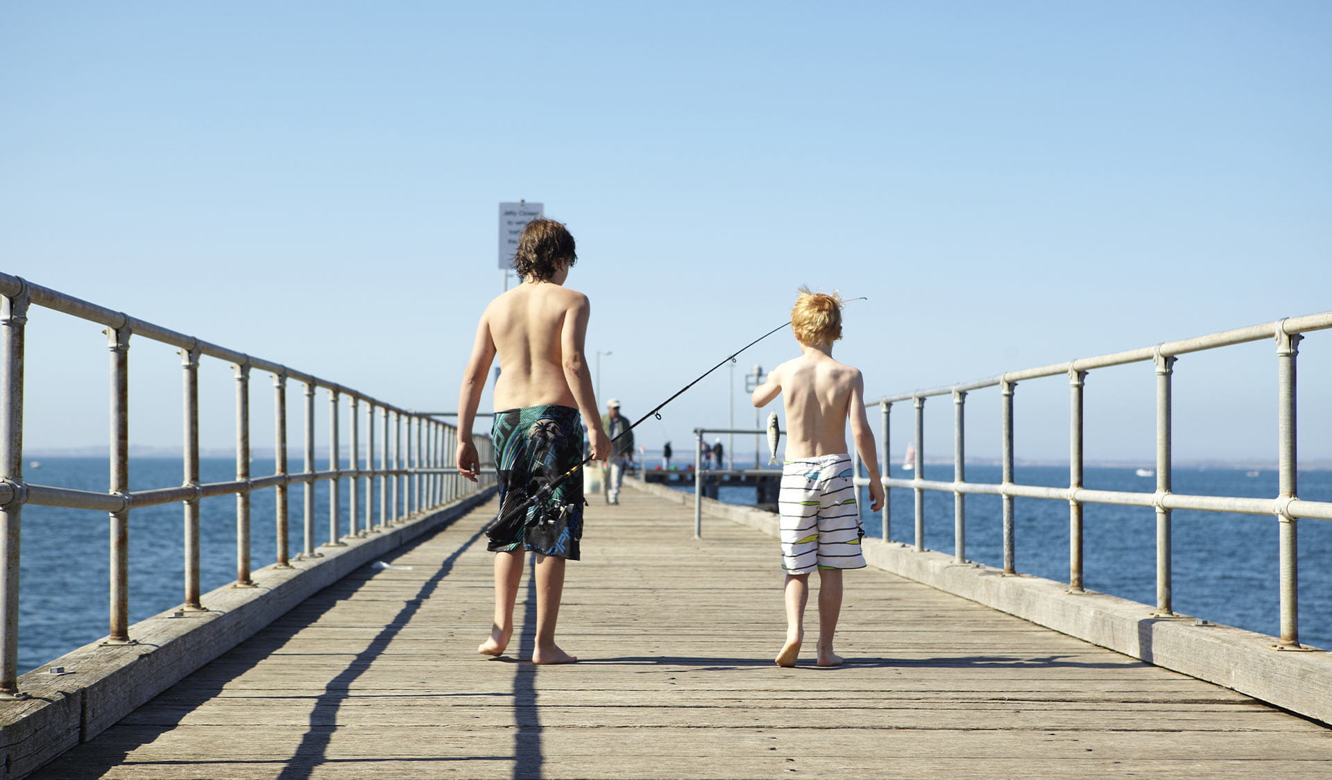 Two children holding fishing rods walk along Flinders Jetty.