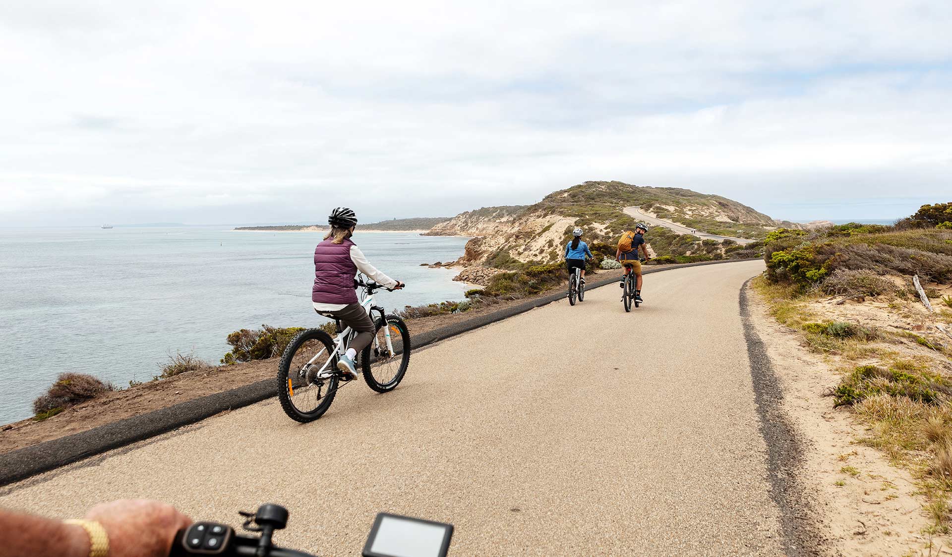 A group of three friends ride bikes overlooking the ocean near the heads to Port Philip Bay.