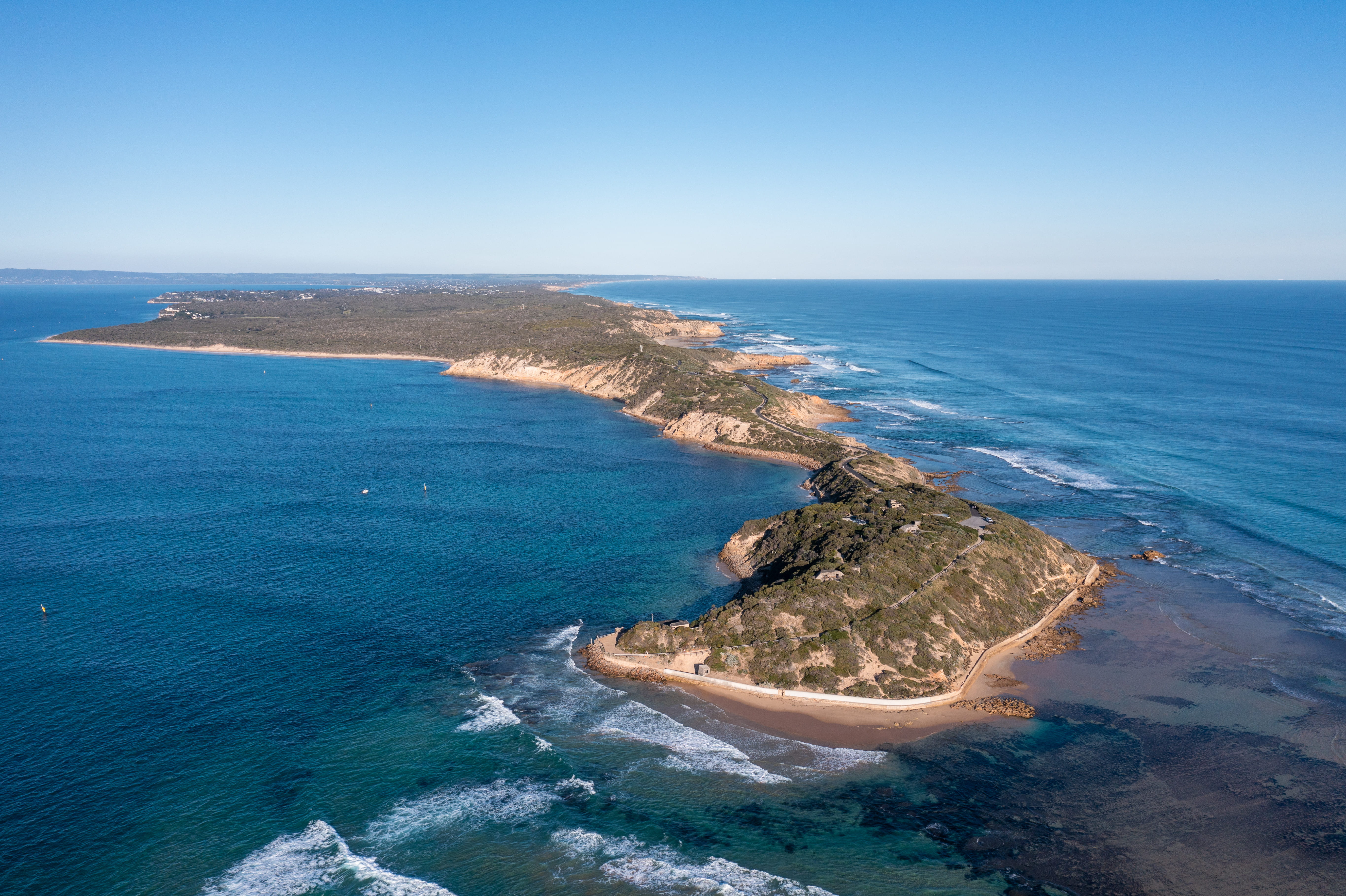 A view of Point Nepean National Park from the sky - a long and narrow strip of land, boarded by beaches and surrounded by blue ocean. 