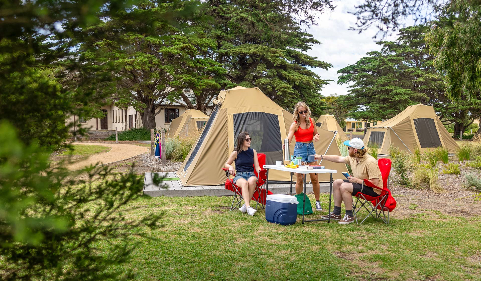 Three people sitting and standing around a camping table in front of a tent.
