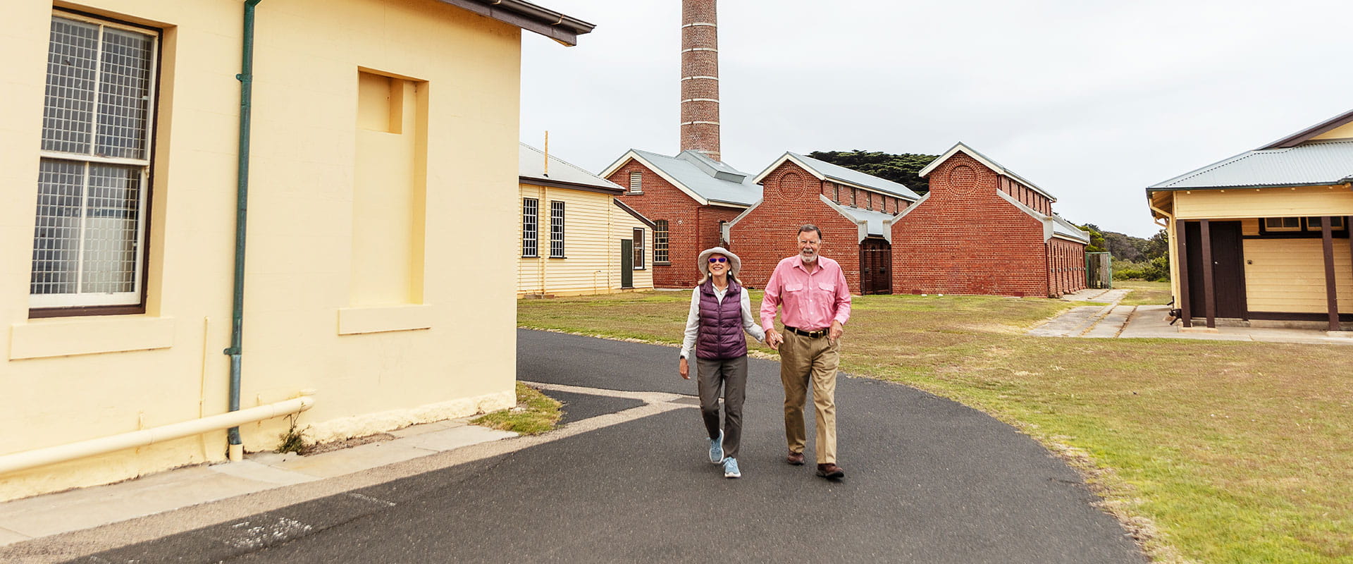 A hetrosexual couple walk hand-in-hand along a sealed path through historic brick buildings