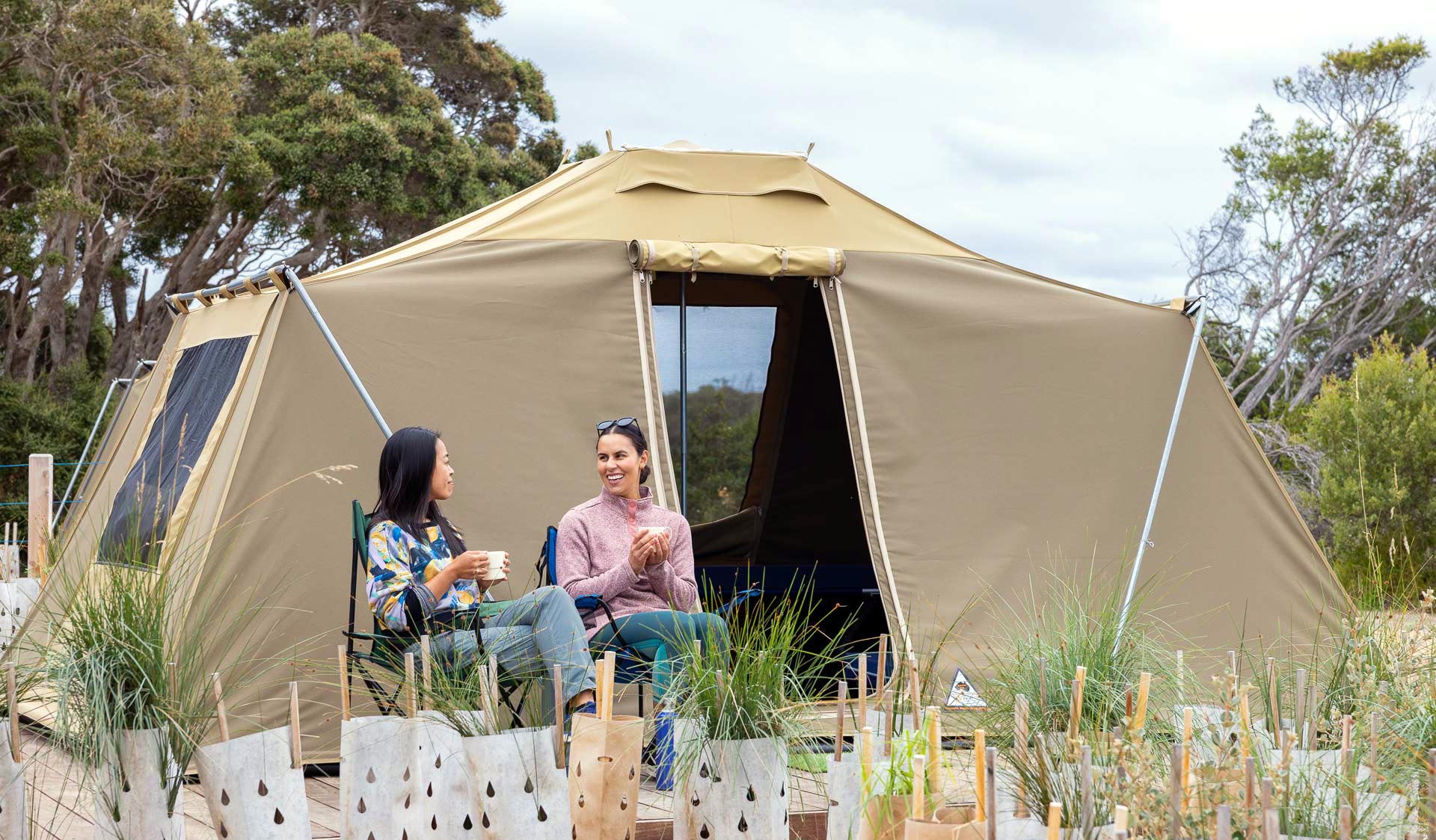 Two women sit and enjoy a cup of tea in front of their tent