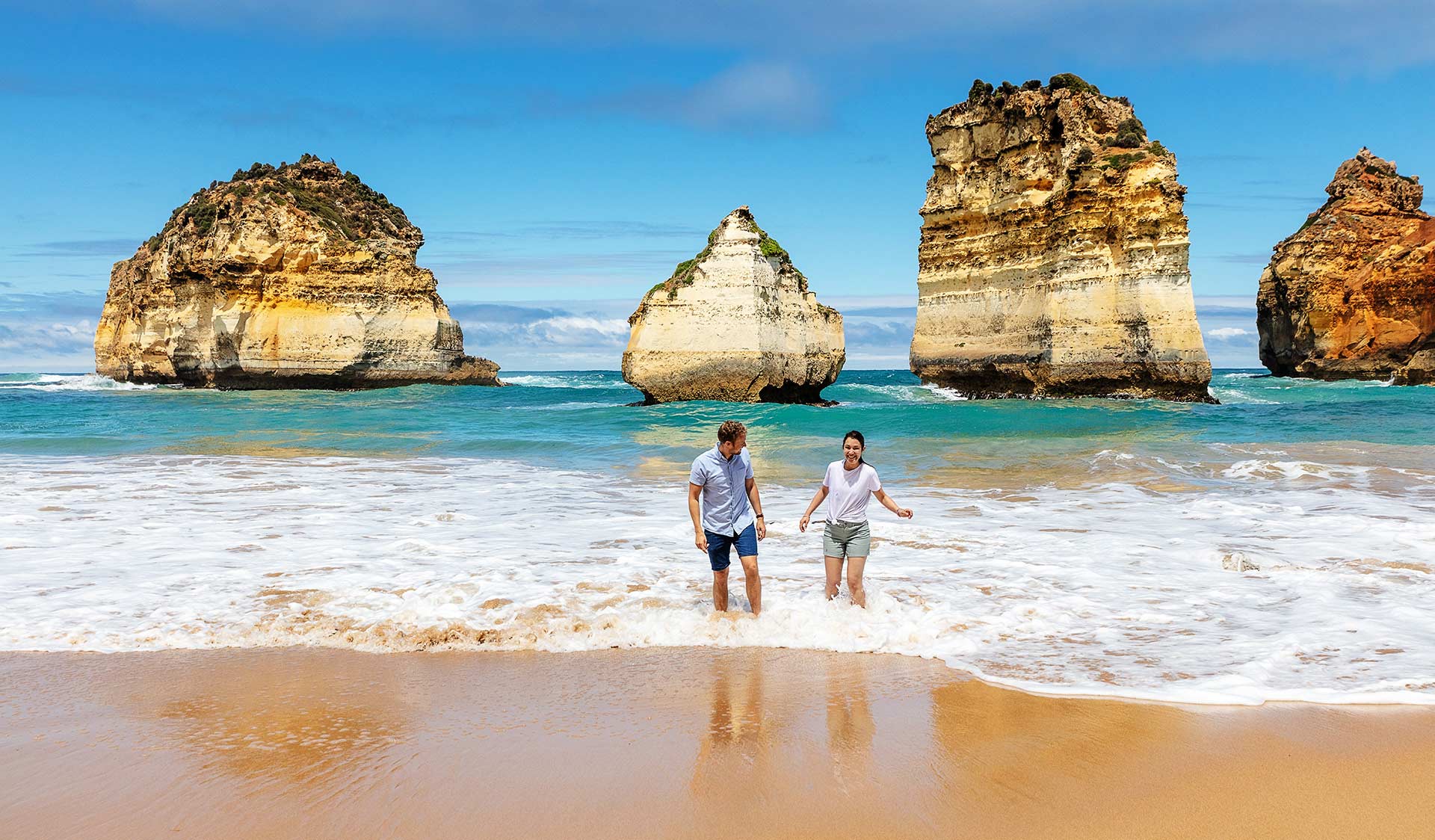 A man and woman play in shallow waters in front of the Twelve Apostles.