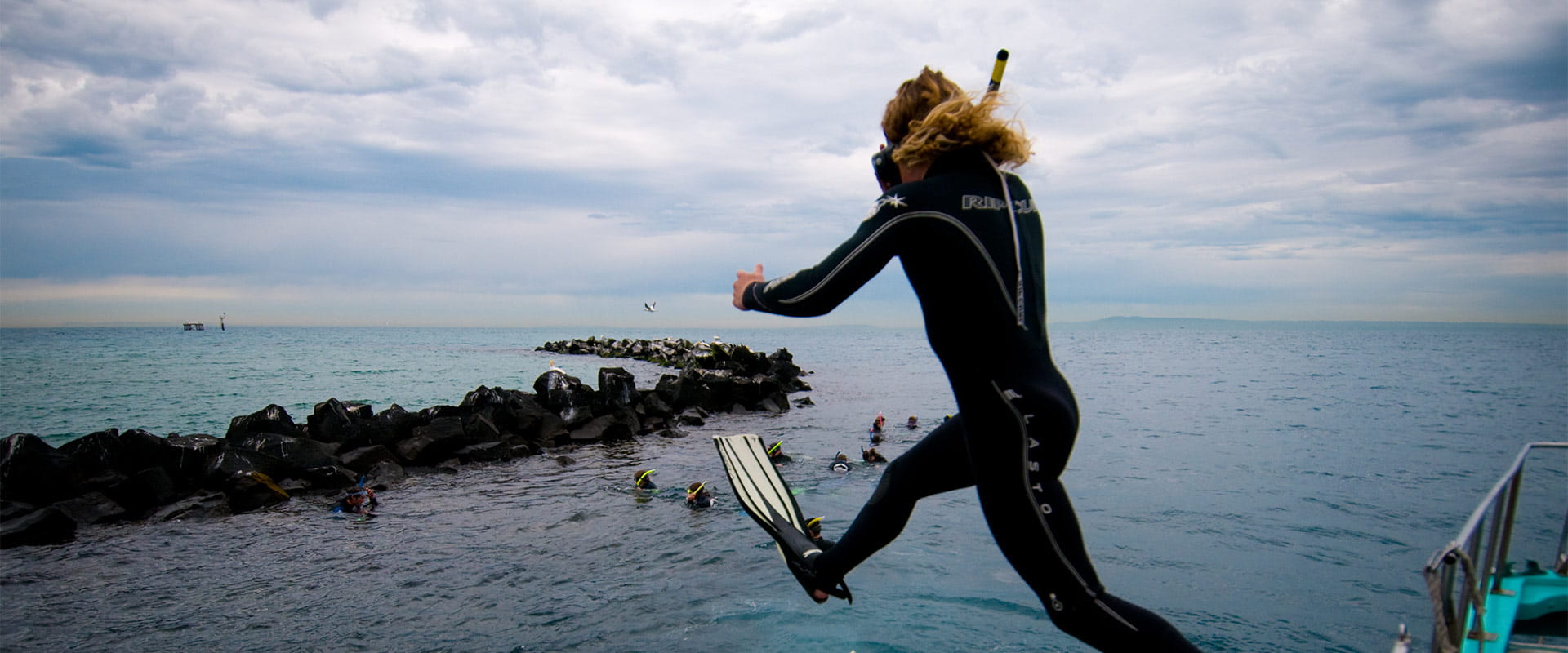 A snorkeller jumps from a boat to join other snorkellers already in the water.