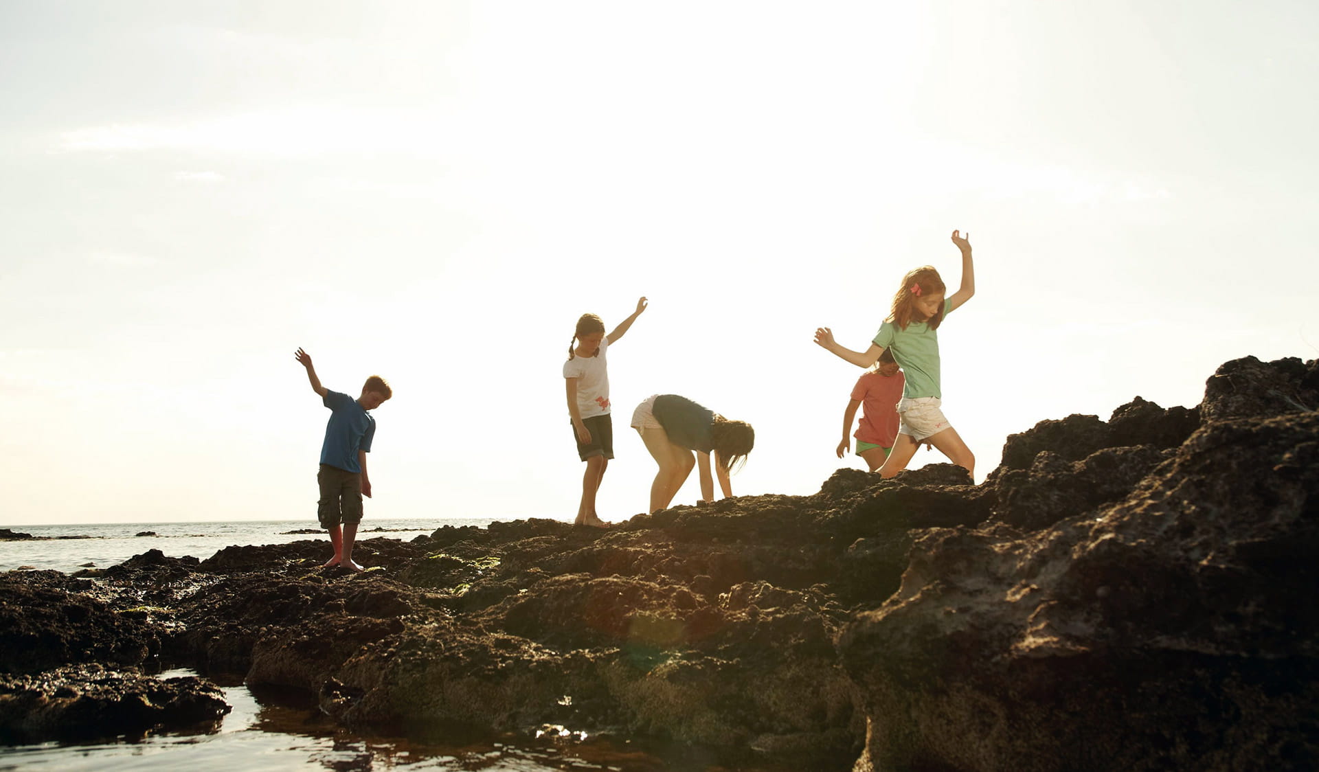 A group of five children play in the rock pools at Ricketts Point late in the afternoon.