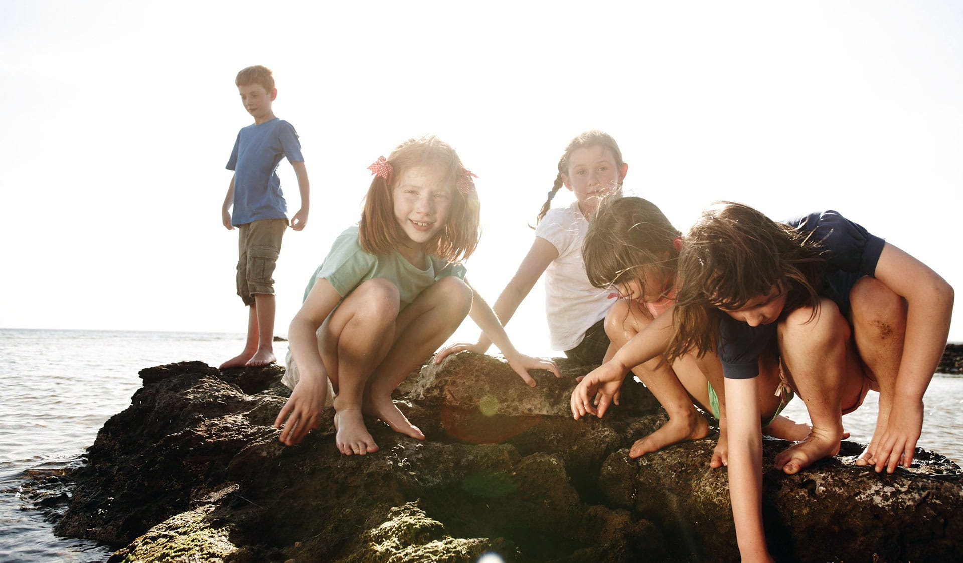 A group of five children play in the rock pools at Ricketts Point late in the afternoon.