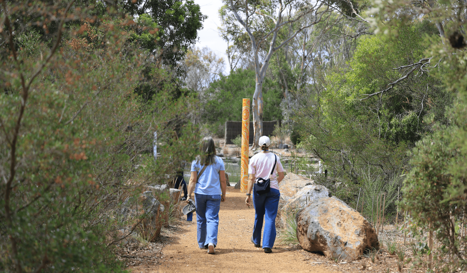 Two people walking along gravel path surrounded by big rocks lining the pathway.