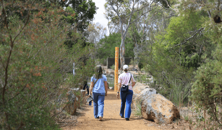 Two people walking along gravel path surrounded by big rocks lining the pathway.