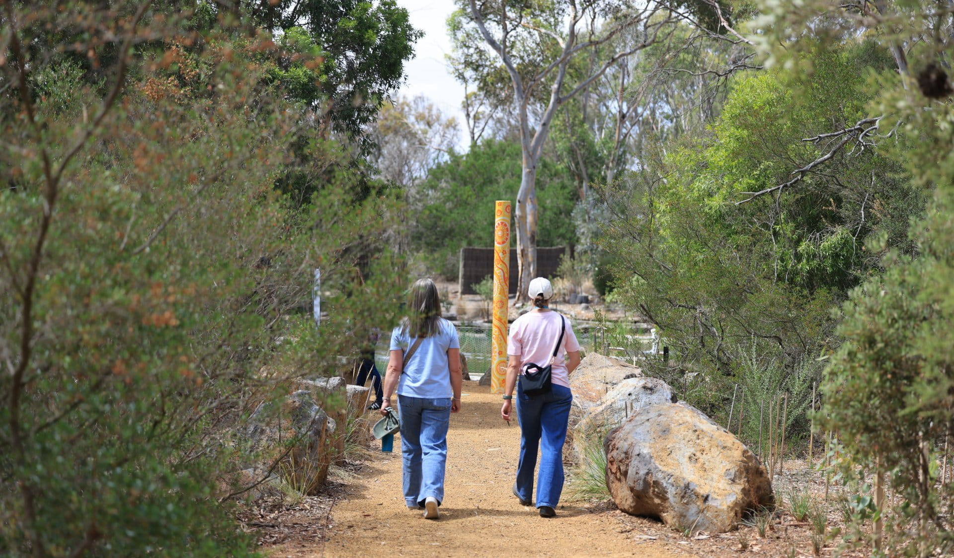 Two people walking into the pathway to sensory garden with art pole between them