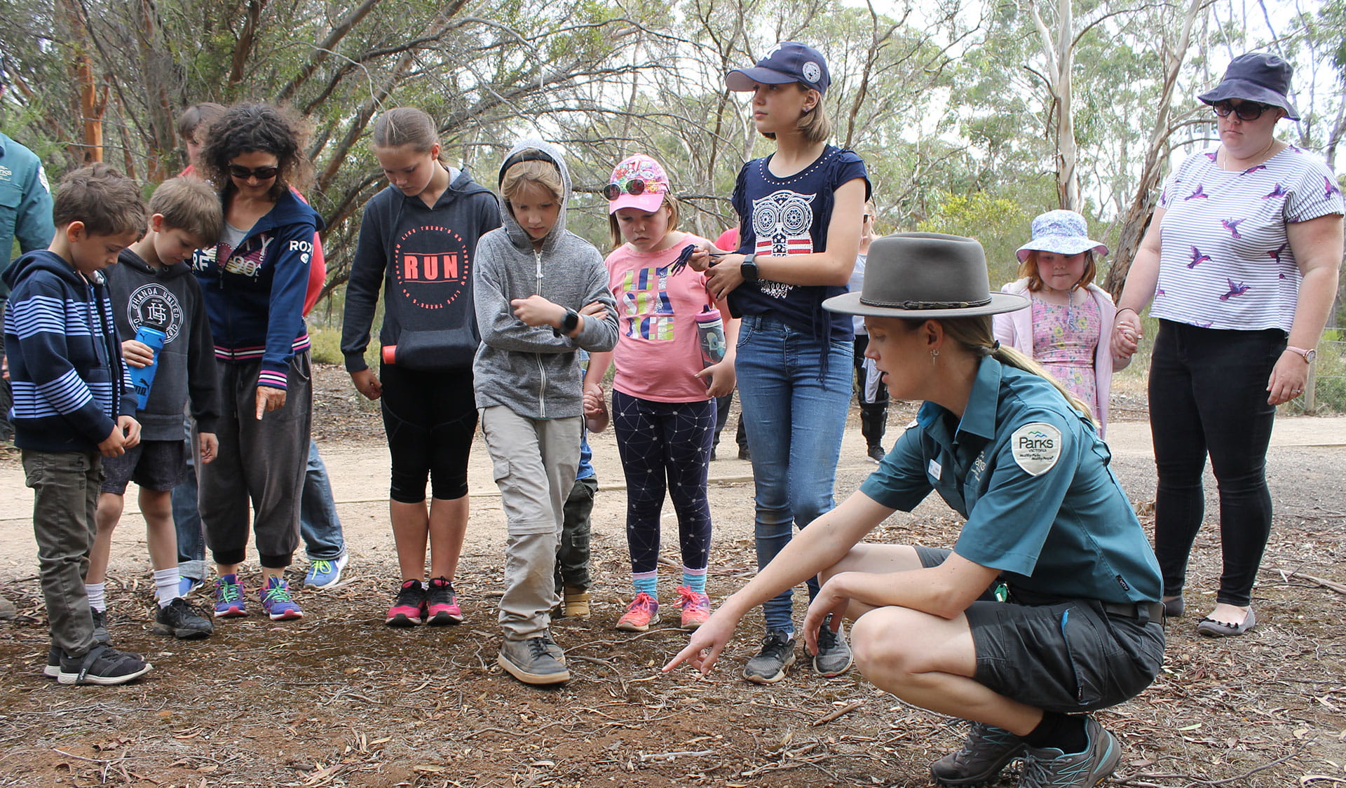 A ranger pointing at the ground, teaching a group of children and adults