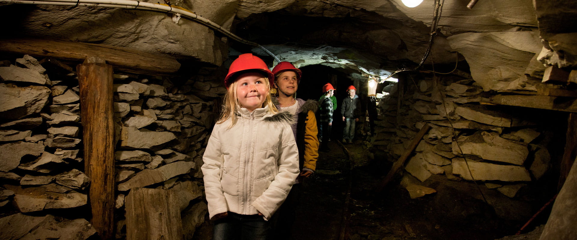Four children wearing hard hats, explore a underground tunnel