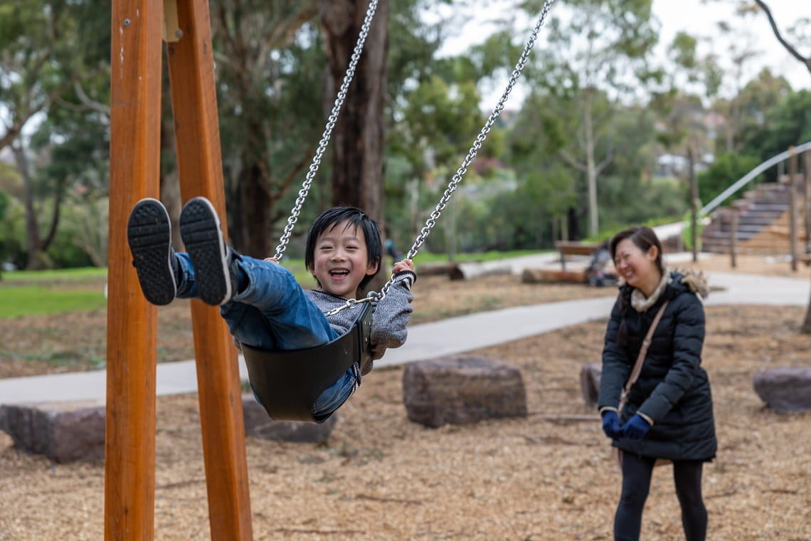 A parent pushes their child on a swing at the Wattle Park playscape.