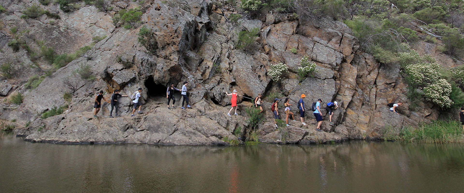A group of walkers carefully make their way along the gorge just above the waterline using a wire guide embedded into the rock to help them along the path.