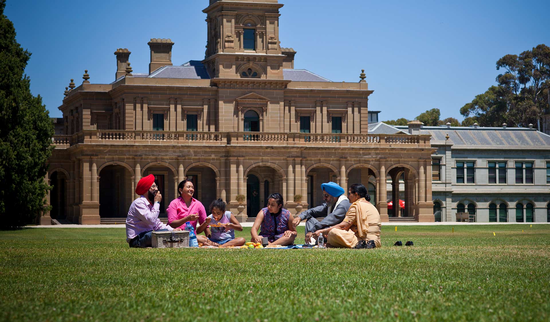 A family share a picnic on the foreground of Werribee Mansion.