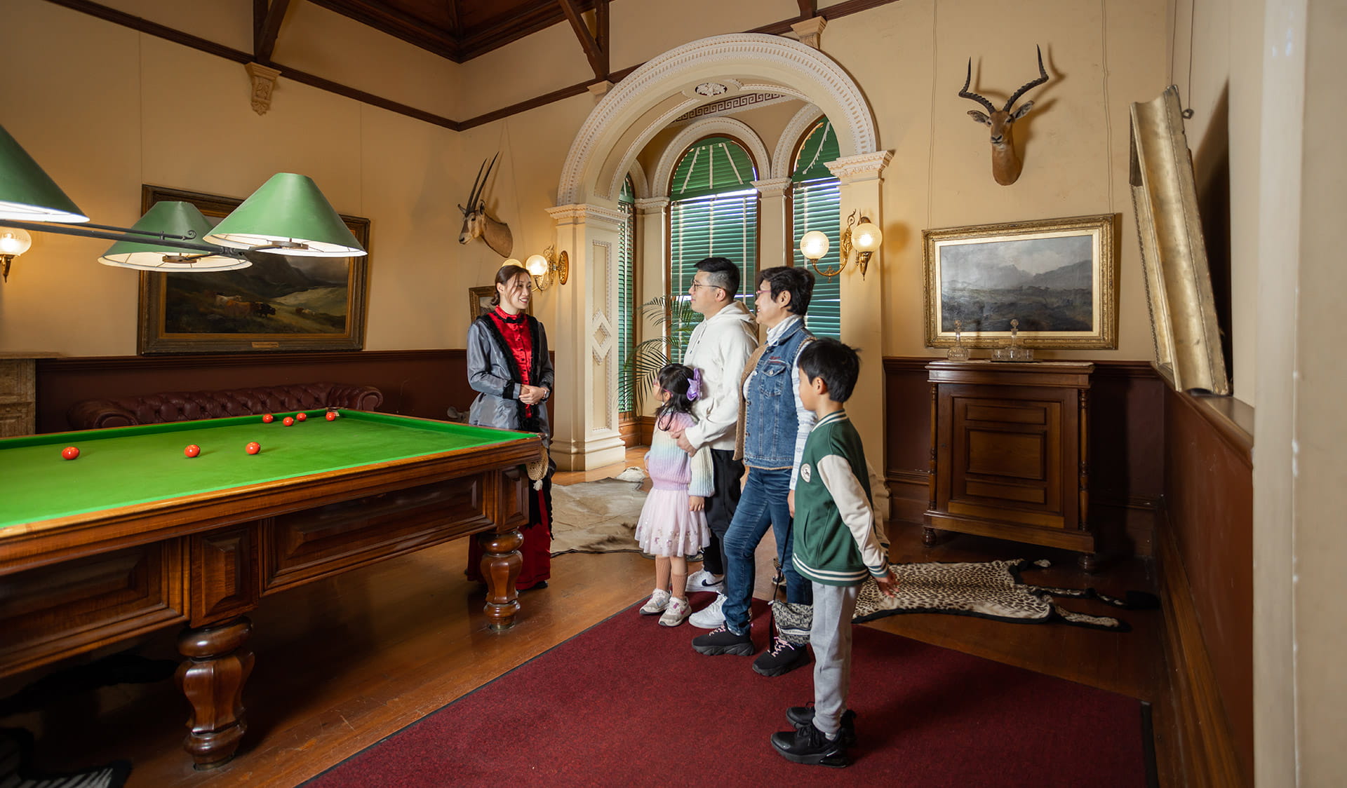 A tour guide in period costume speaking to a family in the Billiard Room at Werribee Mansion.