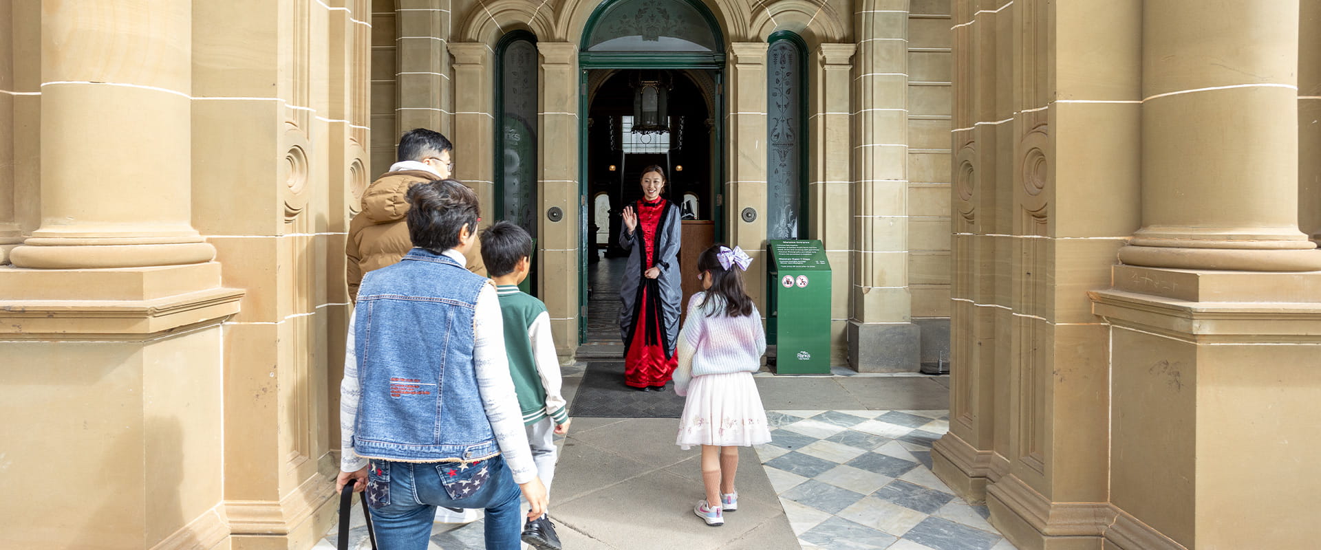 A tour guide in period costume greeting a family as they approach the entrance of the Werribee Mansion.