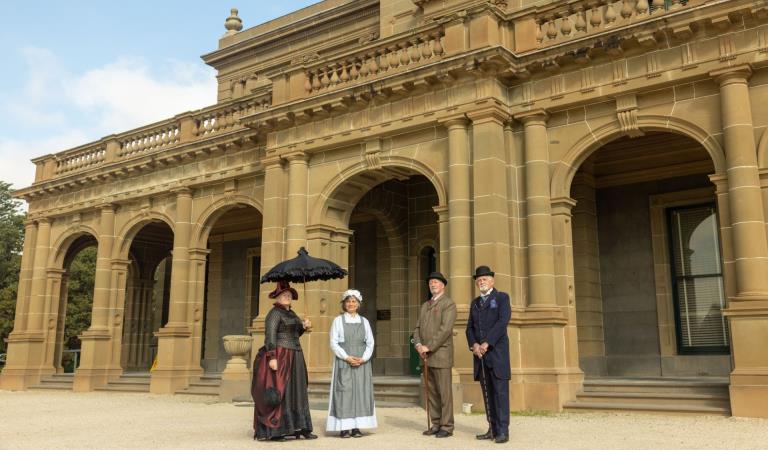 Four people in heritage costumes standing in front of Werribee Mansion.