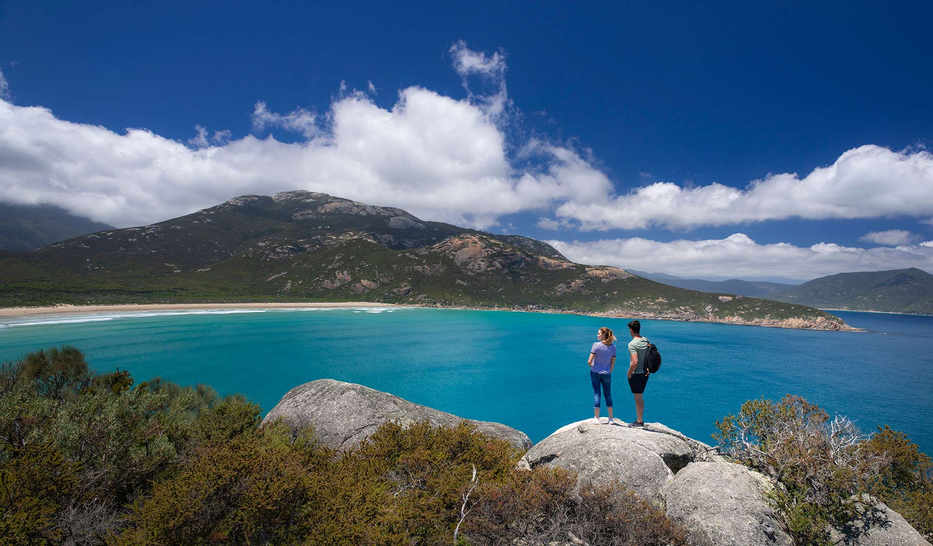 A couple look out over a bay and towards a remote beach on Wilsons Promontory.