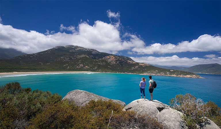 A couple look out over a bay and towards a remote beach on Wilsons Promontory.