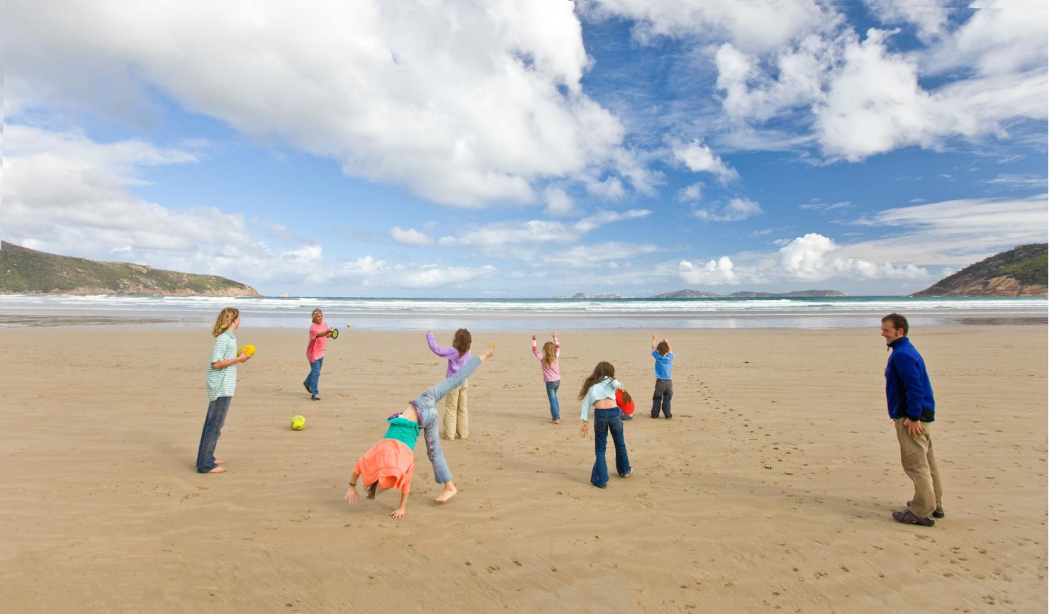 An extended family play with a couple of balls on squeaky beach.