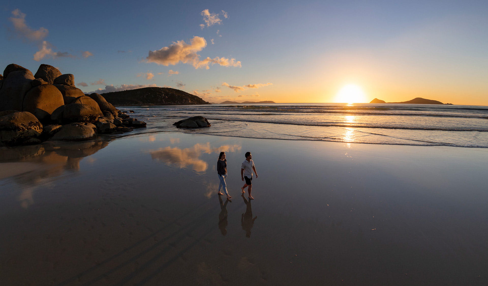 A couple walk across a beach at Wilsons Promontory at sunset.