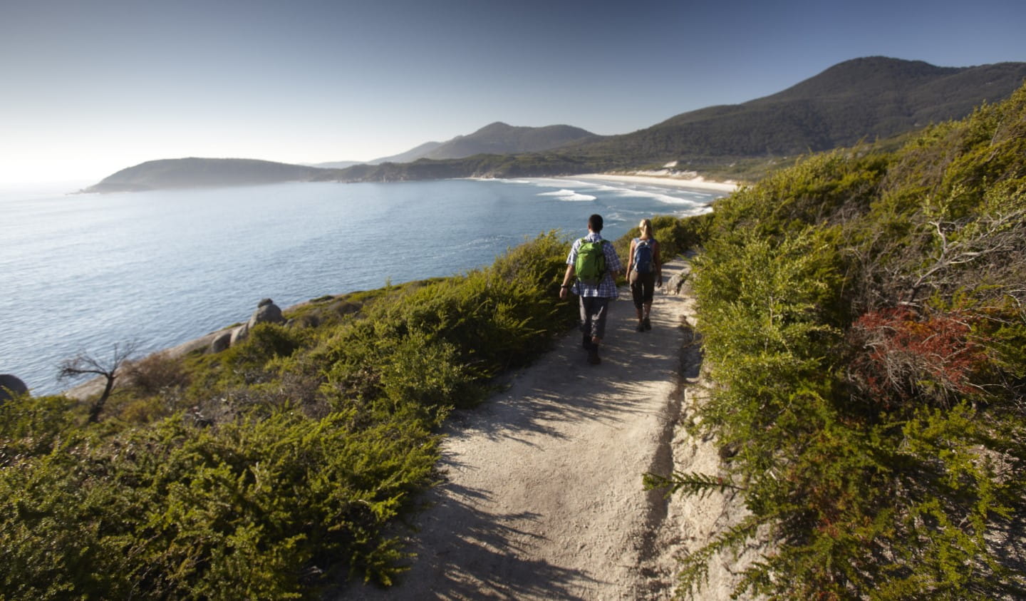 Two people walking towards Squeaky Beach with mountains in the background