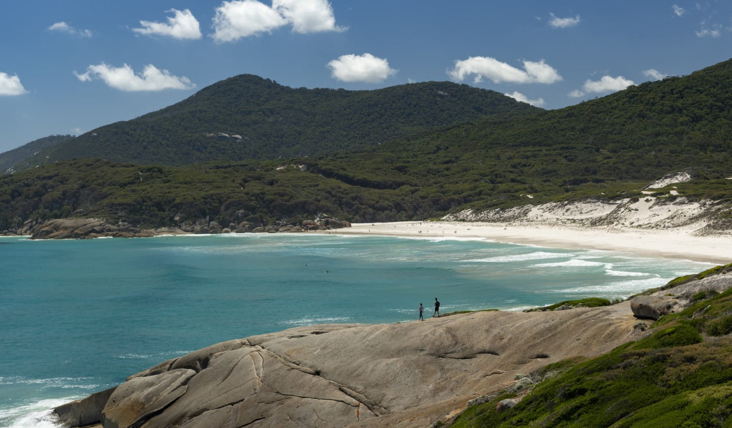 Two people stand on a rock in front of Squeaky Beach