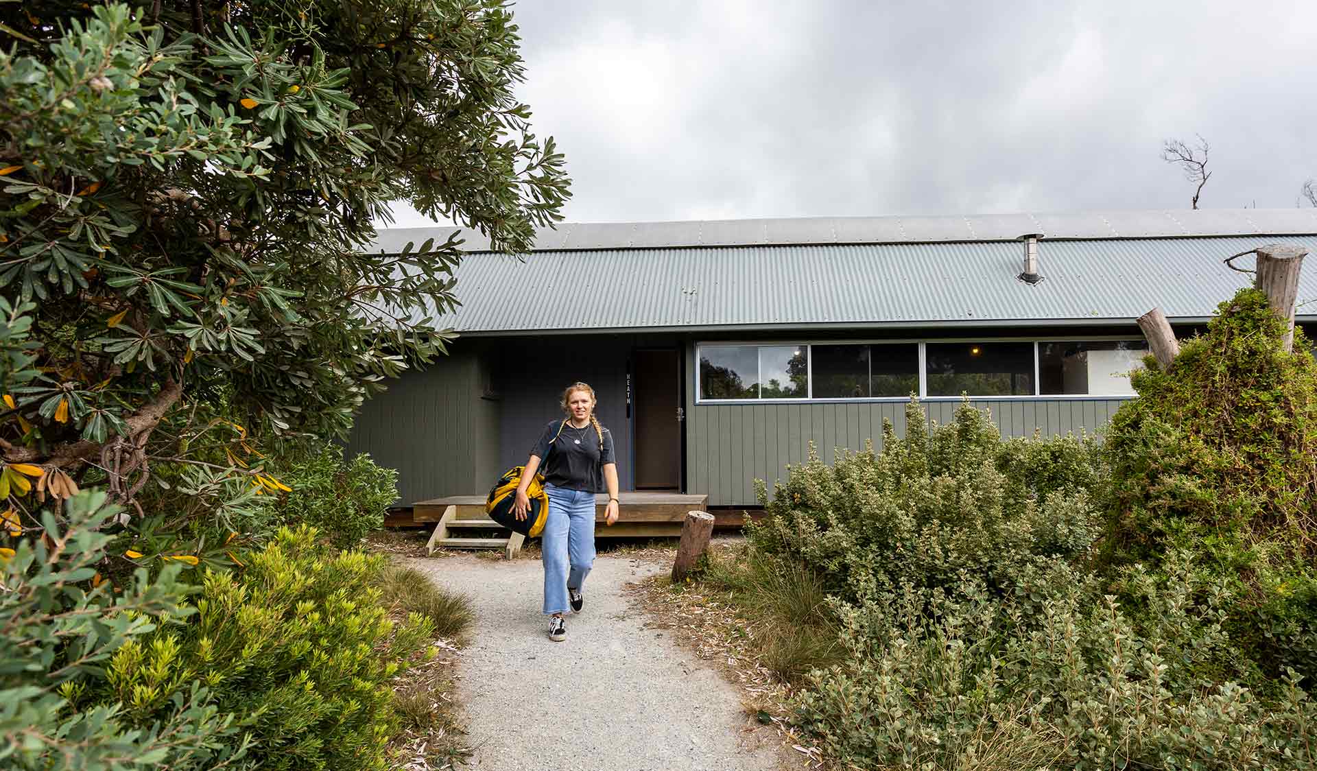 A woman carries a bag and walks away from the entrance to a cabin at Tidal River at Wilsons Promontory National Park