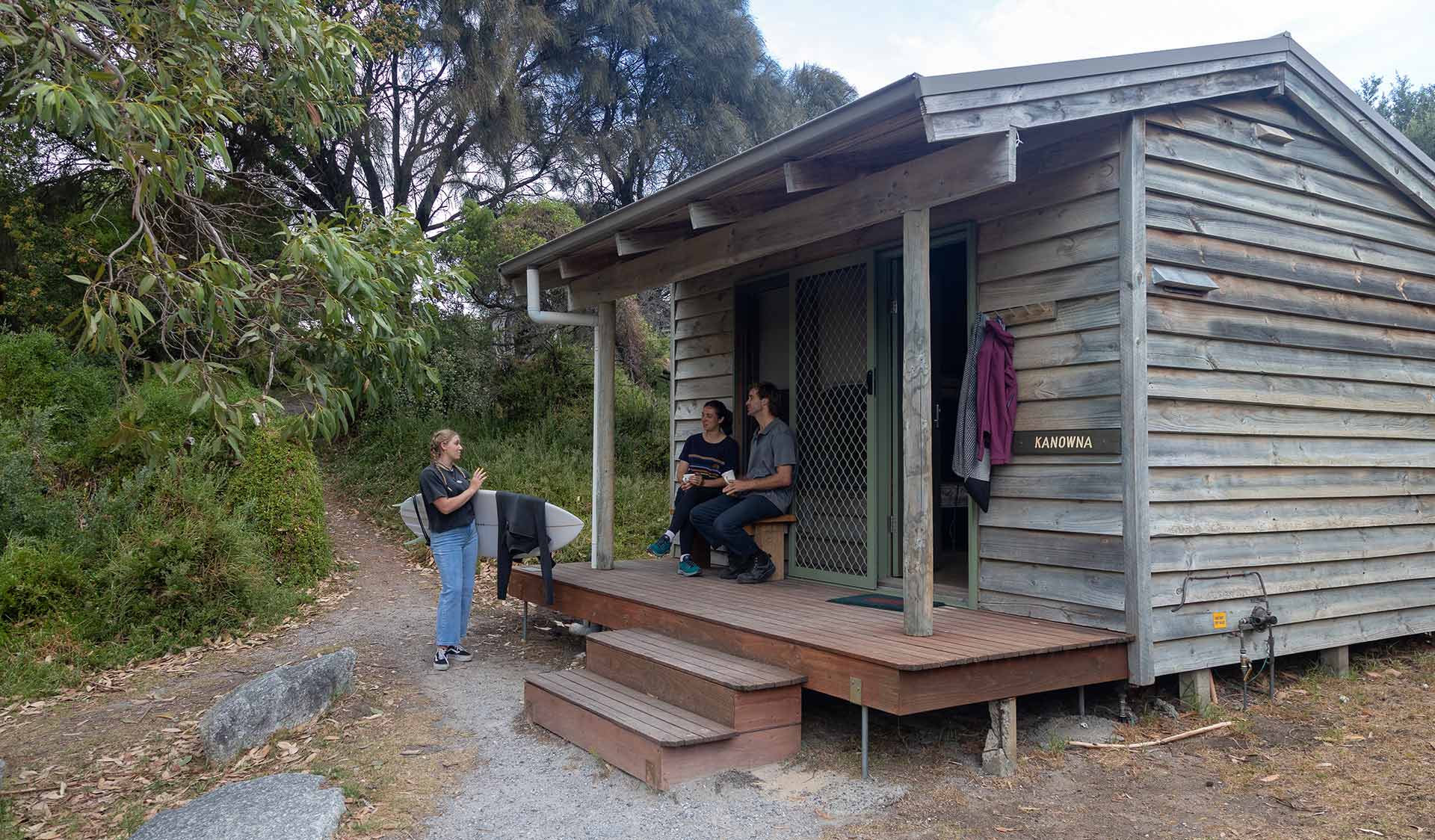 Two friends talk to a female surfer from the porch of a hut at Tidal River at Wilsons Promontory National Park