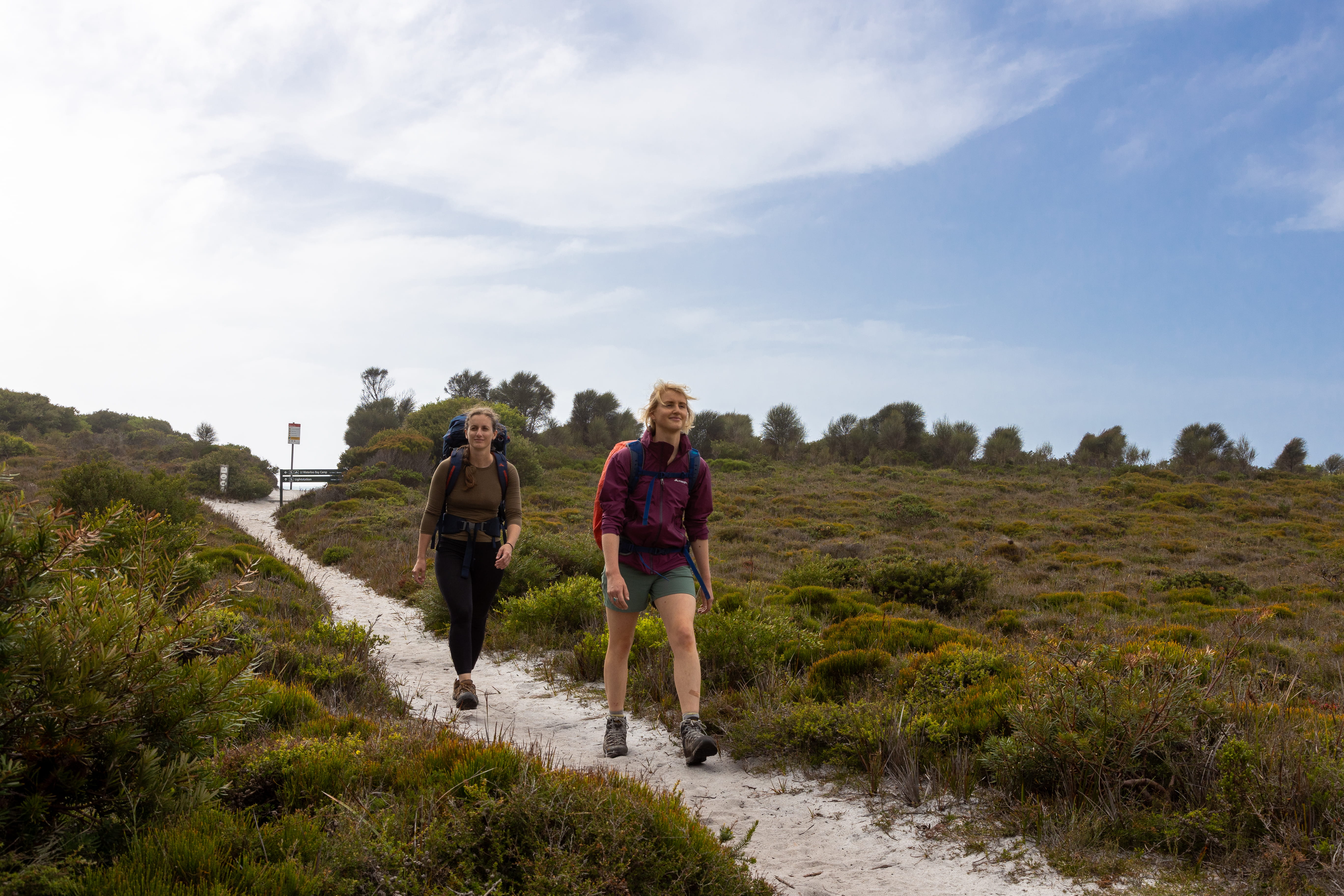 Two women walk along the track next to a coastal marsh on the Southern Circuit hiking trail at Wilsons Promontory National Park