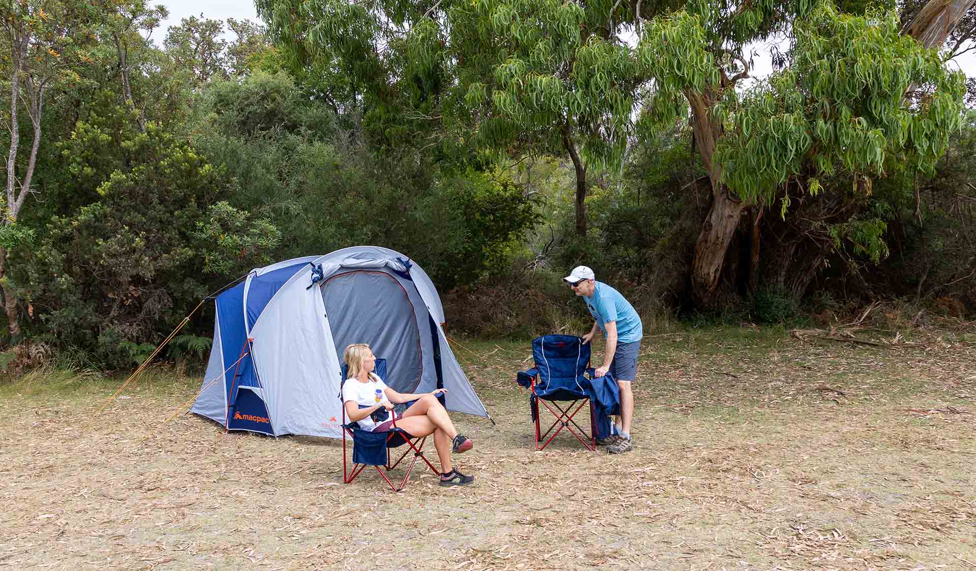 A sets down a camp chair just before sitting down next to an already seated women in front of their tent at Stockyards Campground at WIlsons Promontory National Park