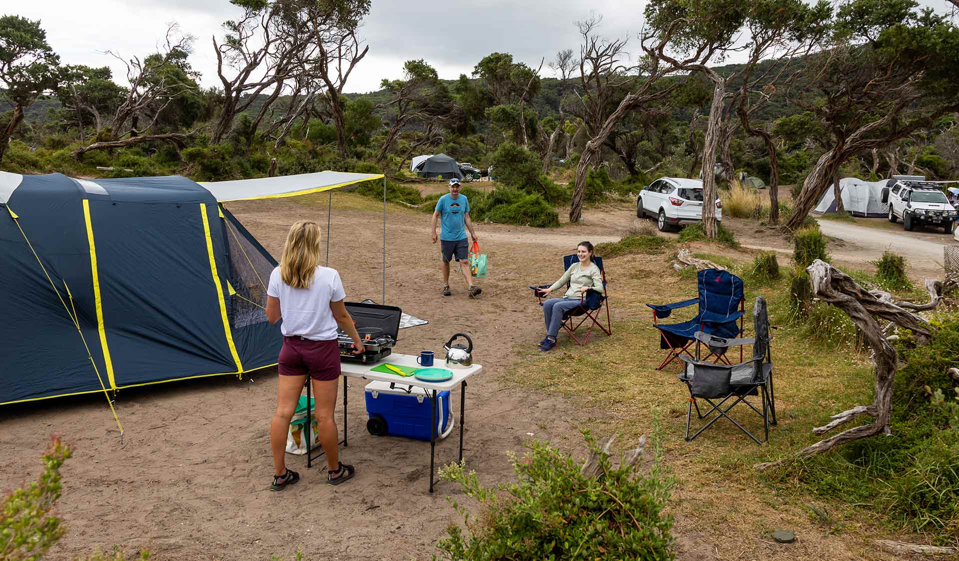 A man walks towards a women who is cooking at a stove next to their tent at Tidal River Campground at Wilsons Promontory National Park