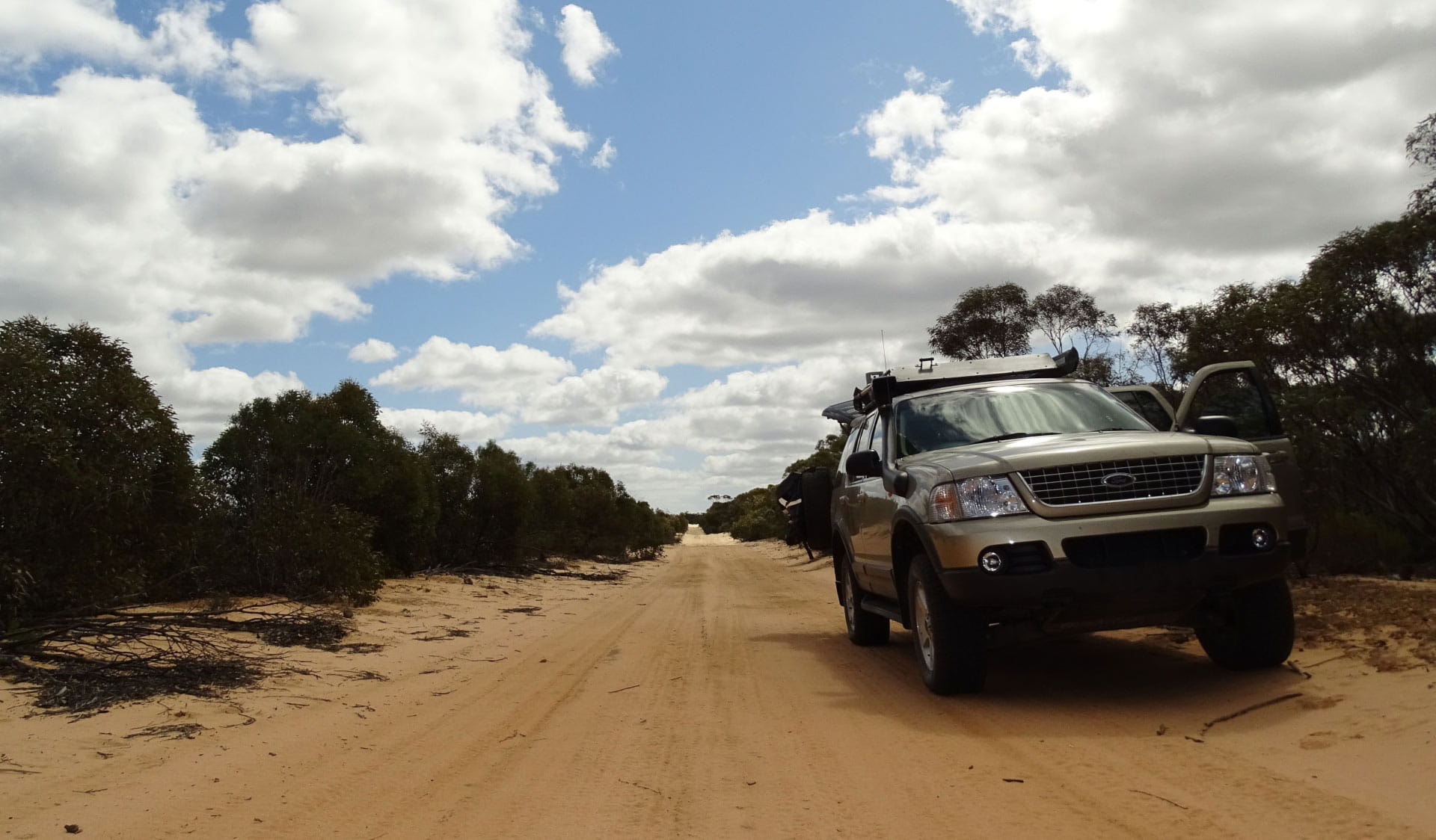 A four wheel drive is parked to the side of a a sandy track at Wyperfeld National Park with a cloudy sky overhead.