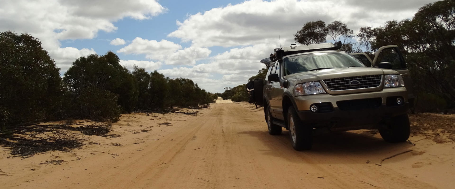 A four wheel drive is parked along a long sandy track in a shrubby rugged bushland