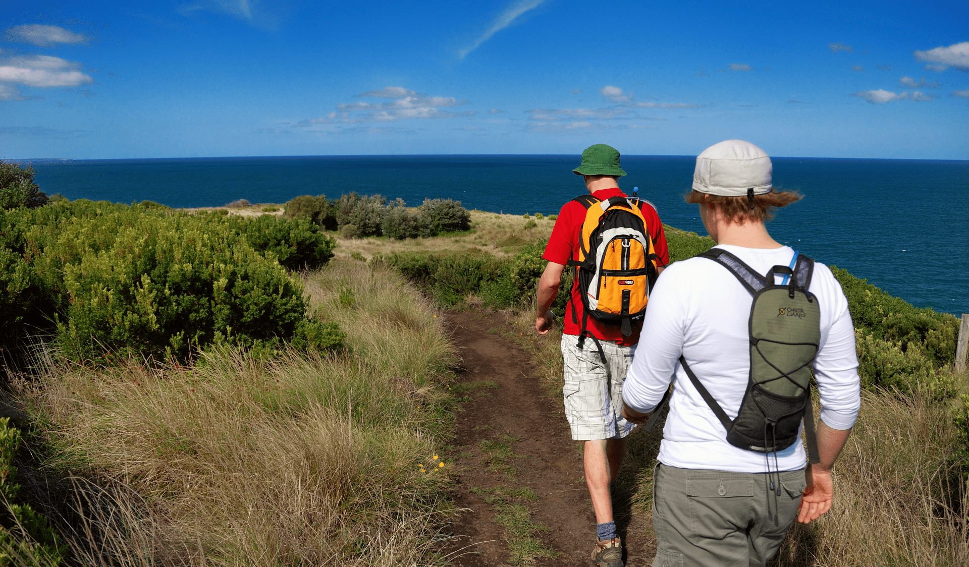 Two men with hats and backpacks walk along the George Bass Coastal Walk