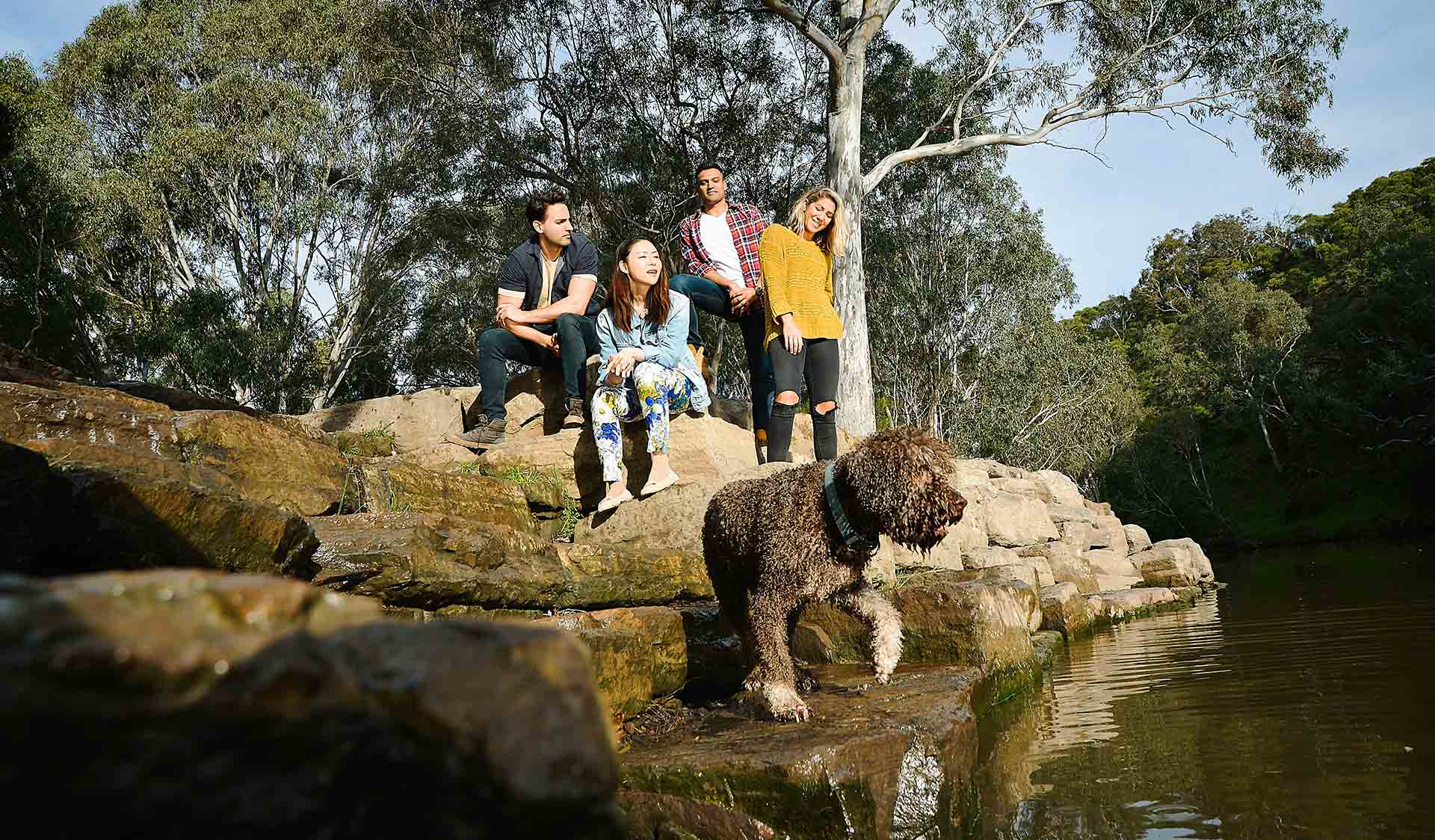 Four friends resting on rocks while watching their dog in front of them by the Yarra River