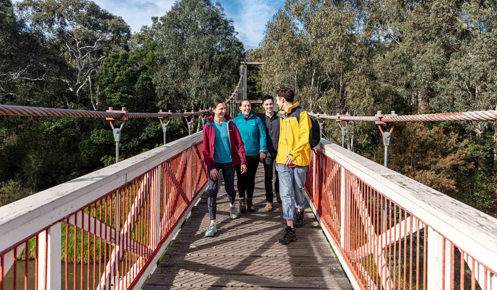 Four friends walk across Kanes Bridge over the Yarra River near Studley Park Boathouse